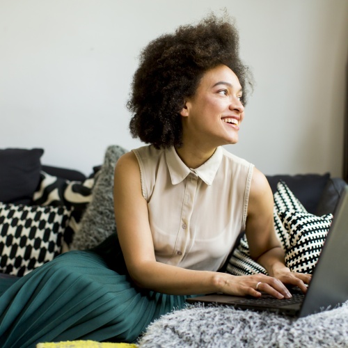 Young Woman With Curly Hair, Uses Laptop And Sitting On The Sofa At Home